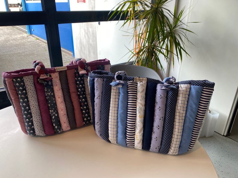 Peut inclure: Deux sacs cabas matelass&eacute;s faits de chutes de tissu. Le sac &agrave; gauche est fait de tissus roses, violets et noirs. Le sac &agrave; droite est fait de tissus bleus, blancs et noirs.