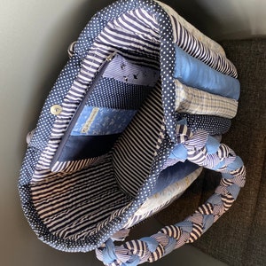 Peut inclure: Un sac fourre-tout matelass&eacute; bleu et blanc avec une poign&eacute;e tress&eacute;e. Le sac est doubl&eacute; d'un tissu ray&eacute; bleu et blanc et poss&egrave;de une poche zipp&eacute;e &agrave; l'int&eacute;rieur. Le sac est rempli de chutes de tissu &agrave; motifs bleus et blancs.