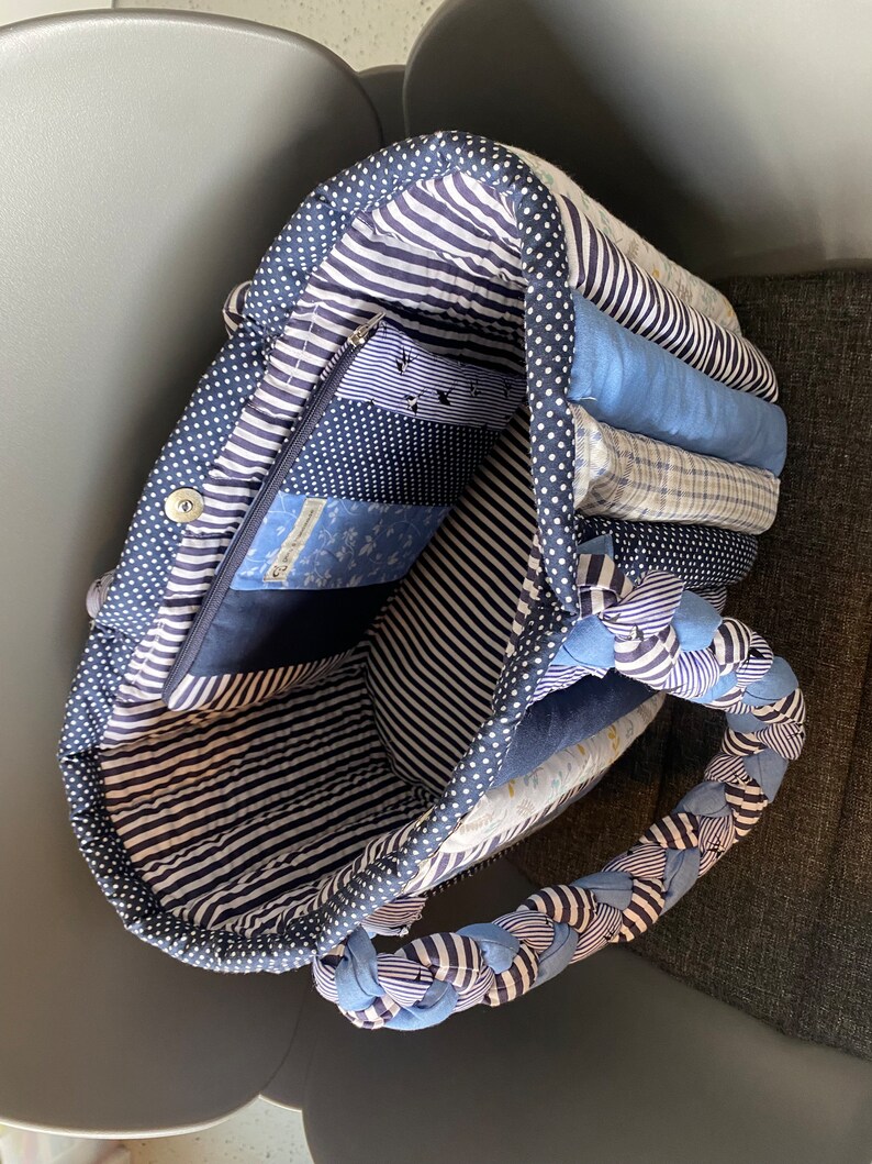 Peut inclure: Un sac fourre-tout matelass&eacute; bleu et blanc avec une poign&eacute;e tress&eacute;e. Le sac est doubl&eacute; d'un tissu ray&eacute; bleu et blanc et poss&egrave;de une poche zipp&eacute;e &agrave; l'int&eacute;rieur. Le sac est rempli de chutes de tissu &agrave; motifs bleus et blancs.