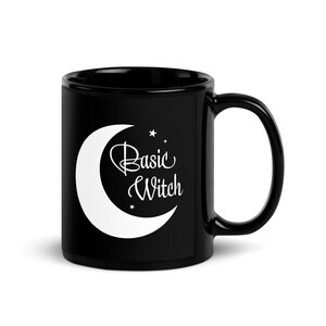 May include: Black ceramic mug with a white crescent moon and the words "Basic Witch". The mug has a curved handle. The design includes small star accents. Suitable for hot or cold drinks. The mug is designed for everyday use.