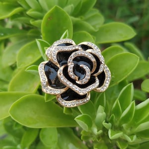 Pode incluir: Um broche preto em forma de rosa com detalhes dourados e strass transparentes.