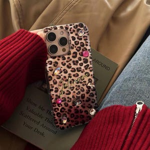 May include: A clear phone case with a leopard print design and rhinestones. The case has the name "Julianne" written in gold lettering.
