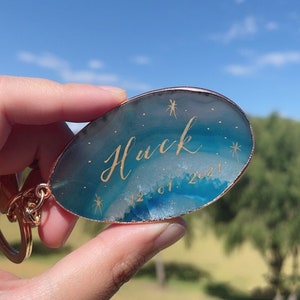 Könnte beinhalten: Ein blauer Achat-Schlüsselanhänger mit einer goldenen Inschrift, die "Huck 12.01.2021" lautet.