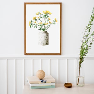 May include: A framed watercolor painting of a bouquet of yellow flowers in a white ceramic vase with a speckled pattern. The vase is sitting on a white surface.