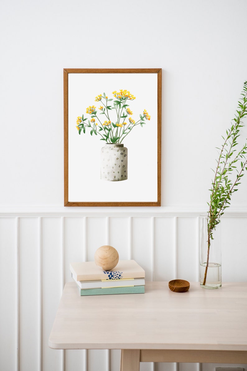 May include: A framed watercolor painting of a bouquet of yellow flowers in a white ceramic vase with a speckled pattern. The vase is sitting on a white surface.
