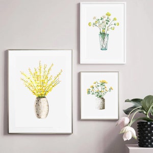 May include: Three framed prints of watercolor paintings of yellow flowers in vases. The prints are hung on a light gray wall.
