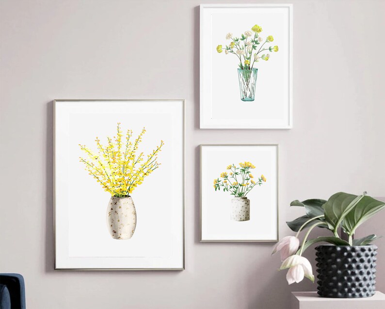 May include: Three framed prints of watercolor paintings of yellow flowers in vases. The prints are hung on a light gray wall.