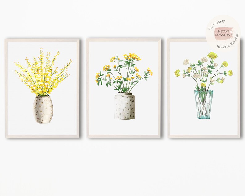 May include: Set of three watercolor prints featuring yellow and white flowers in vases. The prints are framed in white and have a white background.