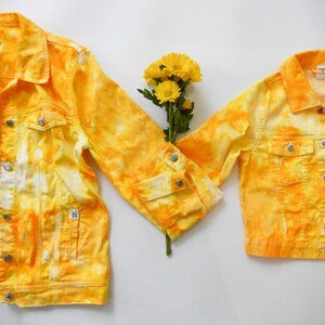 May include: Two yellow tie-dye denim jackets with a bouquet of yellow flowers in the middle.