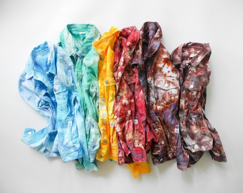 May include: A rainbow of tie-dye denim jackets in blue, green, yellow, red, and brown. The jackets are arranged in a row, with the blue jacket on the left and the brown jacket on the right.