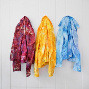 May include: Three denim jackets in different tie-dye patterns: red and purple, yellow and orange, and blue and white.