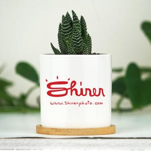 May include: White ceramic planter with a succulent plant and the text "'Shiner' www.Shinerphoto.com" in red.