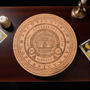 May include: A round wooden Ouija board with engraved letters, numbers, and symbols. The board features a central tree of life design and the words "Yes," "No," and "Rephrase." A candle and tarot cards are in the background.