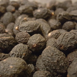 Pode incluir: Uma imagem de close-up de um monte de frutas secas de cor marrom escura e enrugada. A fruta est&aacute; disposta em um padr&atilde;o aleat&oacute;rio, com algumas frutas sobrepostas.