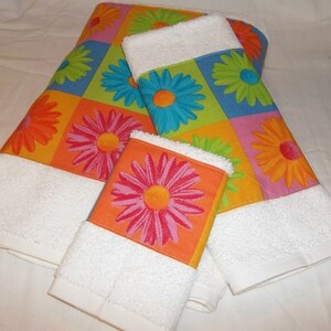 May include: Set of three white bath towels with a colorful floral pattern. The pattern features large, bright flowers in shades of orange, pink, green, blue, and yellow.