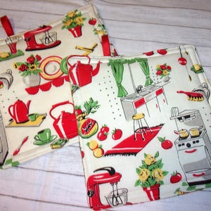 May include: Two square kitchen pot holders with a retro kitchen print. The fabric features red teapots, mixers, and kitchen scenes on a cream background. Each pot holder has a red loop for hanging and a green and white checkered border.