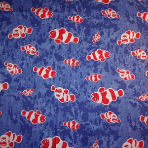 May include: Blue fabric with a pattern of red and white clownfish. The fish are scattered across a blue background with darker blue splotches. The clownfish have smiling faces.