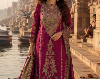 May include: A magenta long-sleeved tunic featuring intricate gold and green embroidery around the neckline and down the front, paired with matching magenta trousers and a coordinating shawl with a green border and gold decorative trim.
