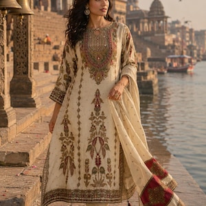 May include: An off-white long-sleeved tunic featuring intricate multi-colored floral embroidery around the neckline and hem, paired with matching straight-leg trousers and a coordinating shawl with a deep red border and tassel accents.
