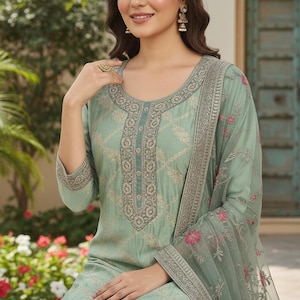May include: A light green embroidered salwar kameez suit. The suit features a detailed pattern on the fabric, with matching embroidery around the neckline and sleeves. A sheer dupatta with pink floral accents completes the ensemble.