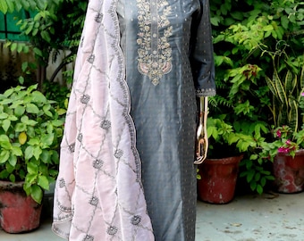 May include: A gray embroidered kurta with a pink embroidered dupatta. The kurta has a round neckline and three-quarter sleeves. The dupatta has a scalloped edge and a delicate floral pattern.