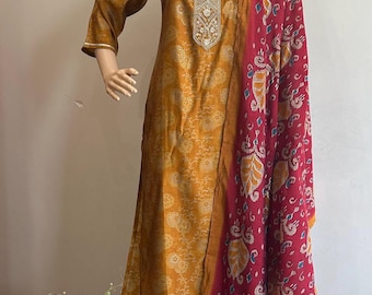 Puede incluir: Una kurta de color amarillo mostaza con bordados dorados y un dupatta con estampado rojo y azul. La kurta tiene una silueta larga y fluida y está hecha de una tela suave y ligera.