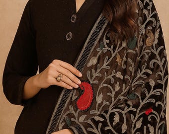 May include: A dark brown outfit comprising a long-sleeved top with decorative buttons and a shawl. The shawl displays an elaborate floral design in brown, grey, red, and green, giving a rich, textured look.