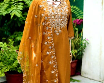 May include: A mustard yellow embroidered kurta with a matching dupatta. The kurta has a V-neckline and is decorated with white floral embroidery. The dupatta is sheer and has a scalloped edge.