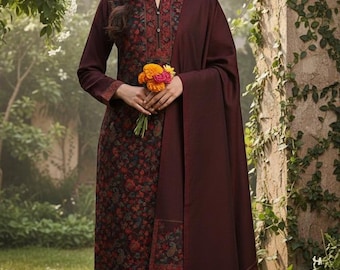 May include: A burgundy salwar kameez with a floral design, long sleeves, and matching trousers. The outfit includes a shawl. The neckline and cuffs feature embroidery. The person is holding a small bouquet of flowers.