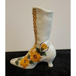 May include: White ceramic boot vase with yellow floral design and gold lacing detail.
