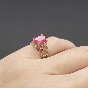 May include: A silver ring with a large, oval-shaped, red gemstone set in a delicate, ornate setting.