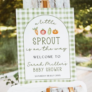 Può includere: Un cartello per baby shower su un cavalletto di legno. Il cartello ha un bordo a quadretti verdi e bianchi. Il testo recita "a little SPROUT is on the way" con illustrazioni di verdure. Dà il benvenuto al baby shower di Sarah Miller.