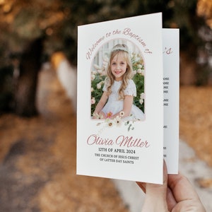 Puede incluir: Una tarjeta blanca con un dise&ntilde;o de arco rosa y una foto de una ni&ntilde;a con un vestido blanco. El texto "Bienvenido al Bautismo de Olivia Miller 12 de abril de 2024 La Iglesia de Jesucristo de los Santos de los &Uacute;ltimos D&iacute;as" est&aacute; impreso en la tarjeta.
