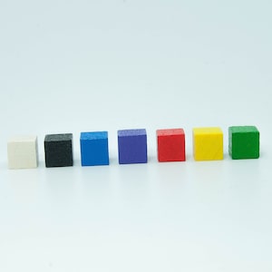 May include: A row of seven small, brightly coloured wooden cubes. The colours are white, black, blue, purple, red, yellow, and green. The cubes are evenly spaced against a white backdrop, creating a simple, clean aesthetic.