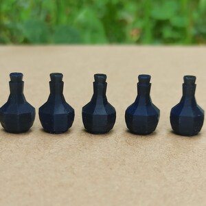 May include: Five small, dark blue, faceted bottles with a bulbous body and a narrow neck. The bottles are arranged in a row on a light brown surface, with a blurred green background. The bottles have a geometric design.