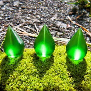 Puede incluir: Tres adornos de vidrio verde en forma de lágrima sobre un lecho de musgo verde.