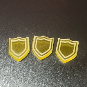 May include: Three yellow plastic shield-shaped tokens. The shields have a white outline.