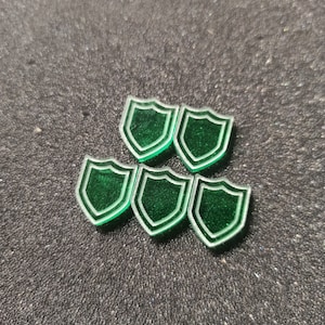 May include: Five green plastic shield tokens with a white outline.