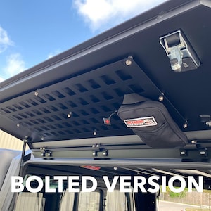 May include: A black metal roof rack with a bolted-on cargo shelf and a black mesh panel. The shelf has a small black pouch attached to it. The text "BOLTED VERSION" is visible in the image.