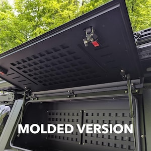 May include: A black truck bed storage box with a molded, black, gridded interior. The lid is open and features a black latch and a red button. The text "MOLDED VERSION" is visible on the front of the box.