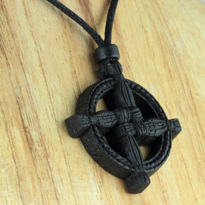 Puede incluir: Un colgante de madera negra con nudo celta en forma de cruz, en un collar de cord&oacute;n negro. El colgante est&aacute; tallado con un dise&ntilde;o de nudo celta.
