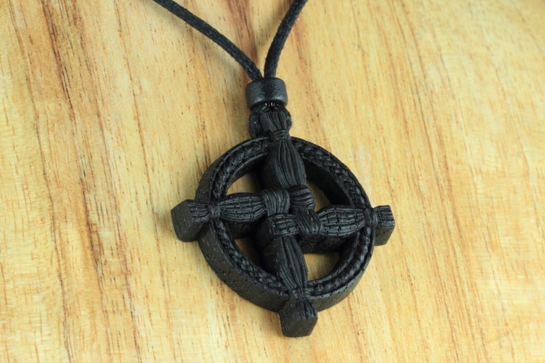 Puede incluir: Collar con colgante de nudo celta de madera negra con cord&oacute;n negro. El colgante es redondo con un dise&ntilde;o de cruz.