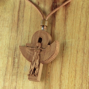 Peut inclure: Un collier en bois avec un pendentif sculpté représentant le symbole égyptien de l'ankh avec une déesse ailée à l'intérieur. Le collier est fait d'un cordon en cuir brun.
