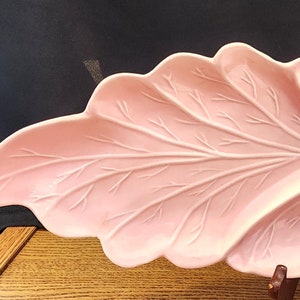 Puede incluir: Un plato de servir de cerámica rosa con forma de hoja con tres secciones. El plato tiene un patrón de hoja detallado.