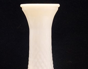May include: A white, diamond-patterned vase with a flared top. The vase has a bulbous base and tapers upwards. The surface has a textured, raised diamond pattern. The vase is made of a solid, opaque material and is set against a dark background.
