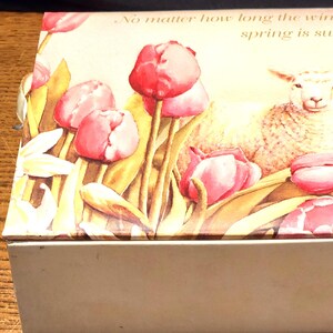 May include: A rectangular box with a lid featuring a spring-themed design. The lid displays pink tulips, a lamb, and the quote "No matter how long the winter, spring is sure to follow." The box has a light beige base.