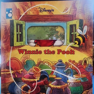 Puede incluir: Un libro infantil de Winnie de Pooh con una función emergente. La portada muestra a Winnie de Pooh asomándose por una ventana con una abeja volando. El título es "Winnie de Pooh La abeja gorda" y el libro está etiquetado como "Un libro de marionetas".