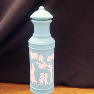 Può includere: Una bottiglia di ceramica blu chiaro con un disegno bianco di un albero e figure. La bottiglia ha un tappo a cupola e una base con un design scanalato.