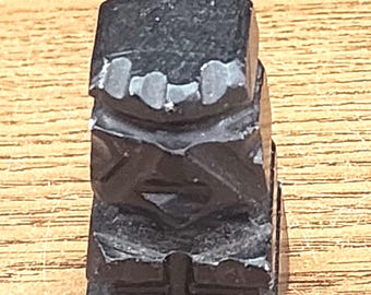 May include: A small, black, carved stone statue of a person with a simple design. The statue is about 2 inches tall and has a smooth, polished finish.