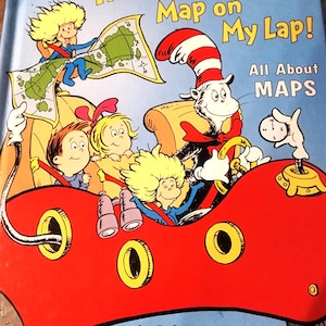 Puede incluir: Portada de libro infantil titulada "There's a Map on My Lap!" con el Gato en el Sombrero conduciendo un coche rojo con pasajeros. La portada incluye ilustraciones de mapas y personajes, con texto que indica que trata sobre mapas.